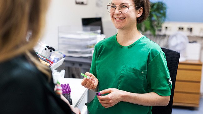 Vihreään työpaitaan pukeutunut työntekijä Mehiläisen lääkäriasemalla.