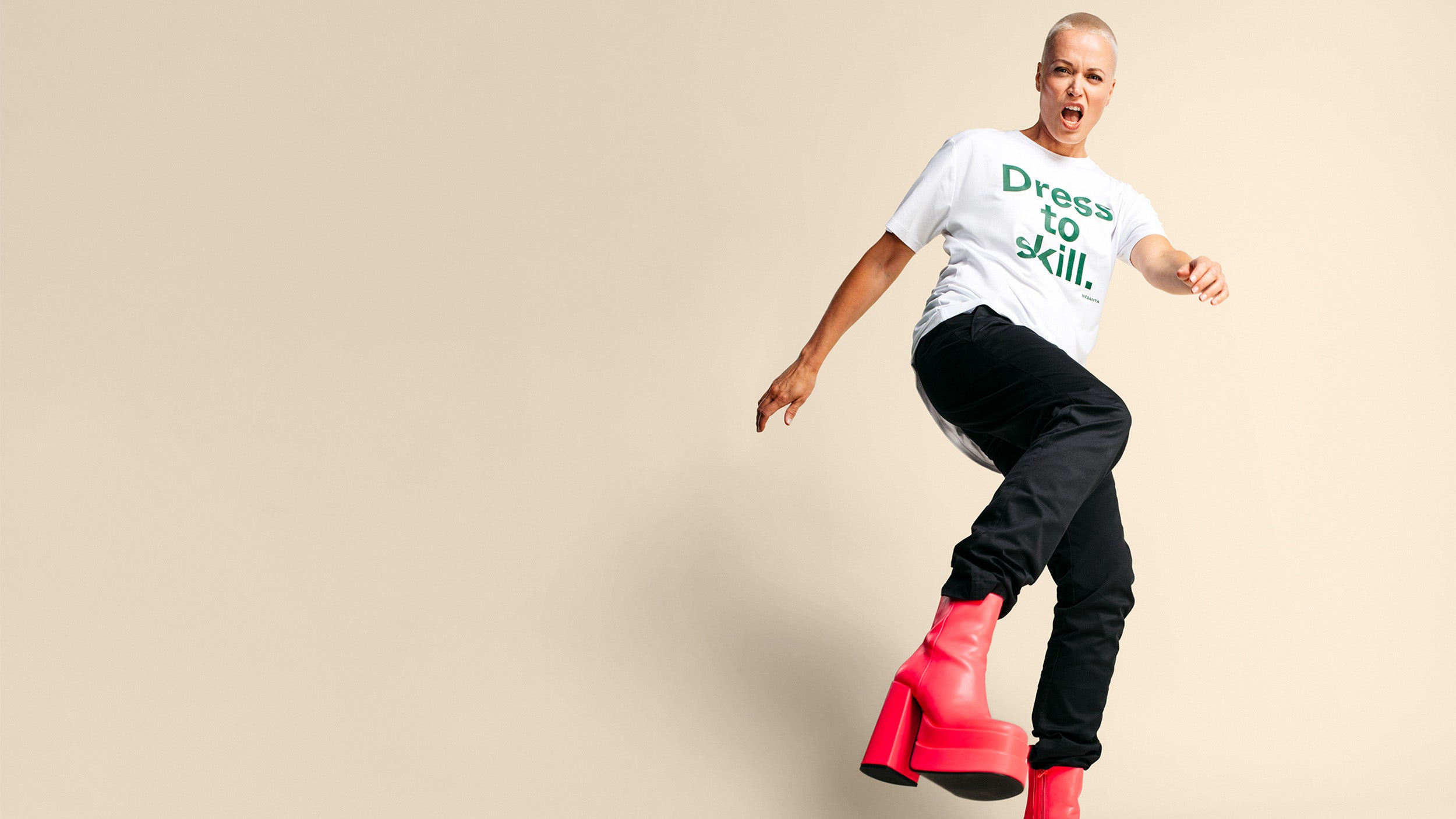 Nainen valkoisessa Medantan "Dress to Skill"-paidassa, housuissa ja punaisissa korkokengissä potkaisemassa kohti kameraa.