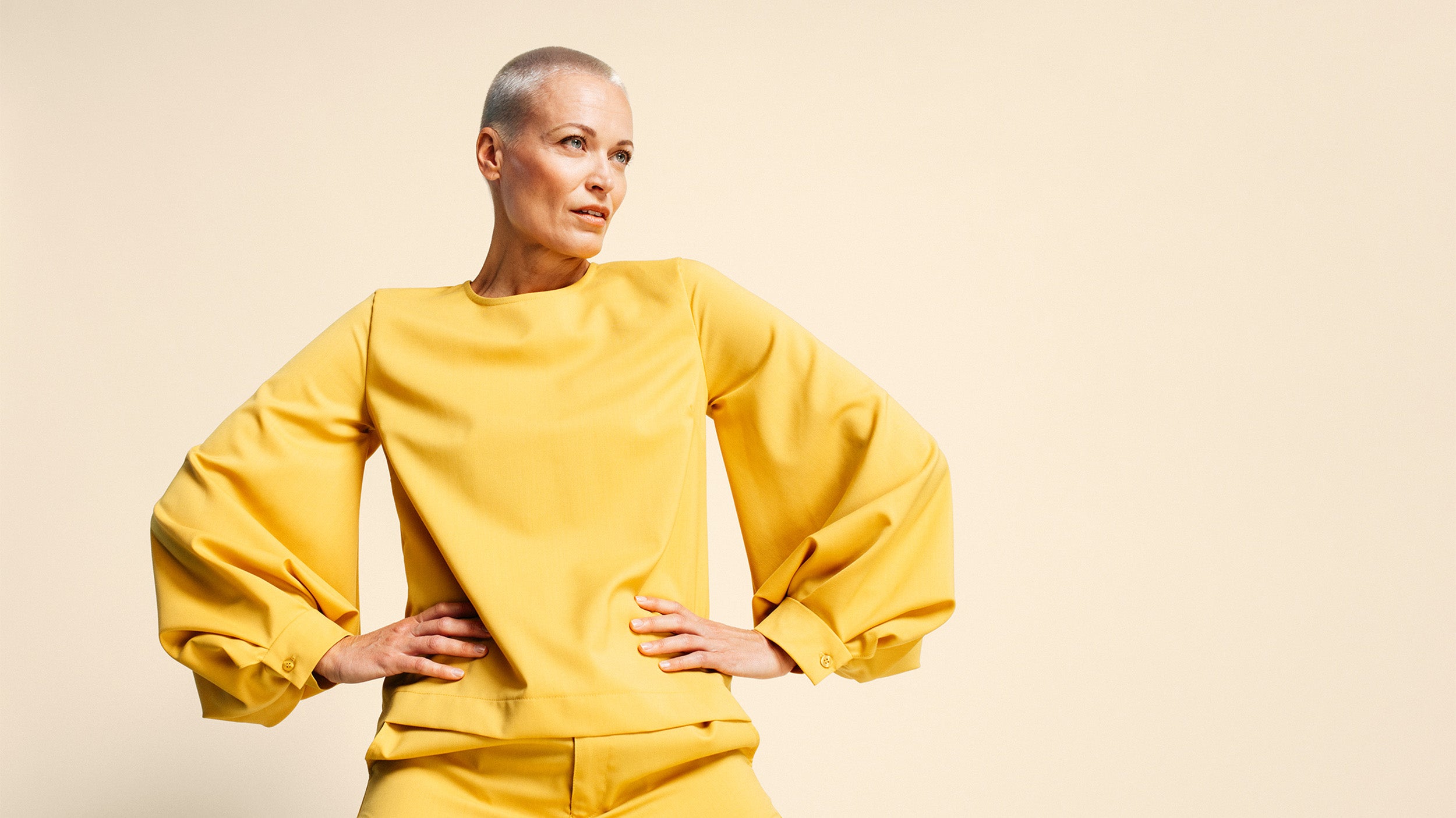 Siilitukkainen nainen keltaisissa housuissa ja keltaisessa leveähihaisessa paidassa.