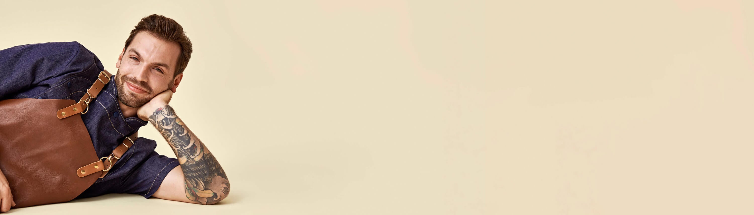 Kokin vaatteet, eli kokintakki ja ruskea nahkaesiliina kokin päällä. Beige tausta.