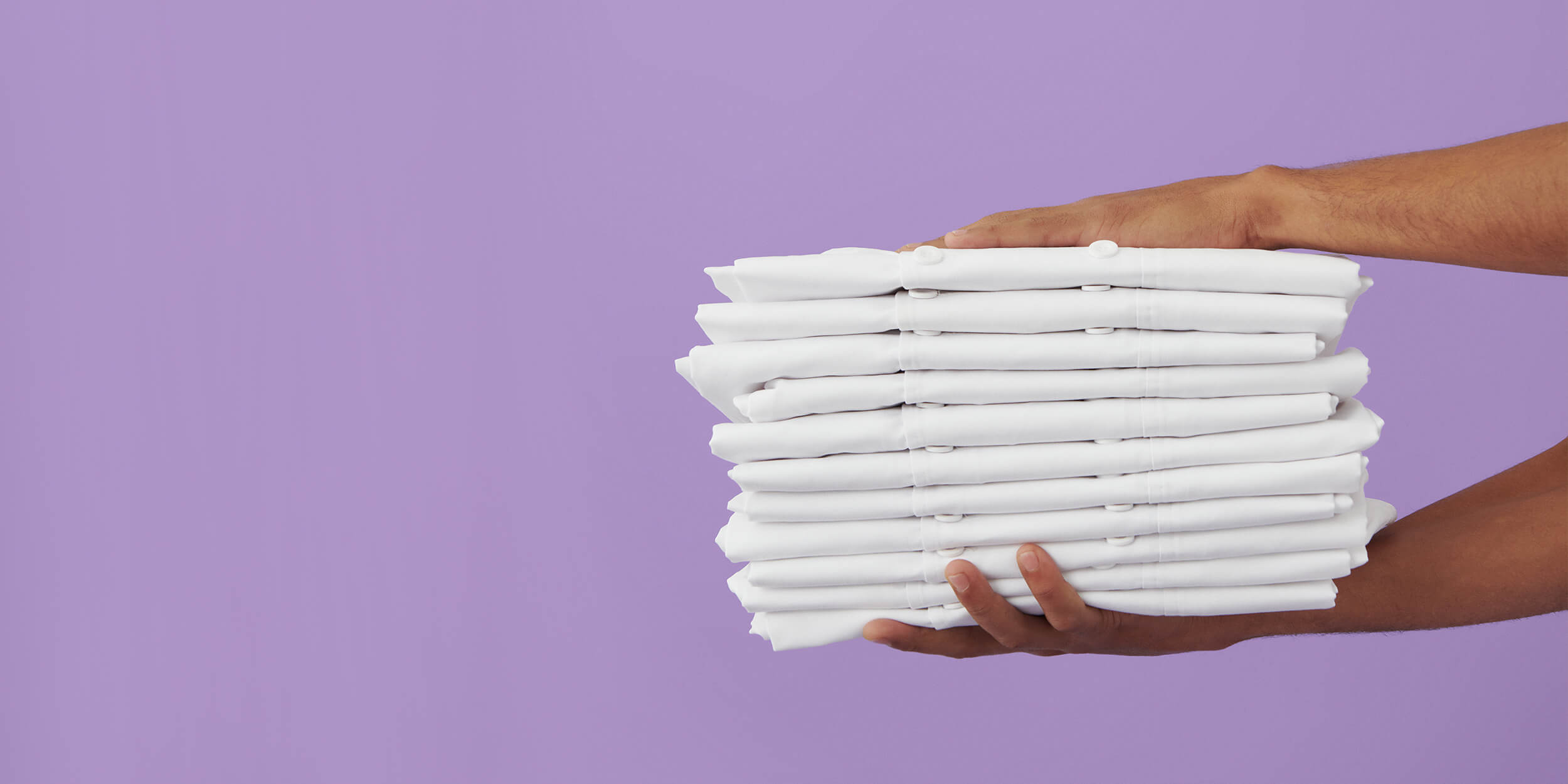 Pino puhtaita, viikattuja, valkoisia työpaitoja käsiparin pitämänä violetilla taustalla.